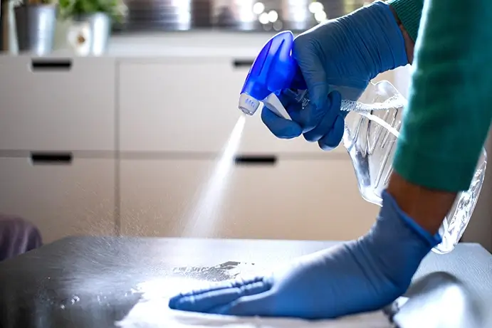 Une personne en gant bleu nettoie une substance blanche sur une table.