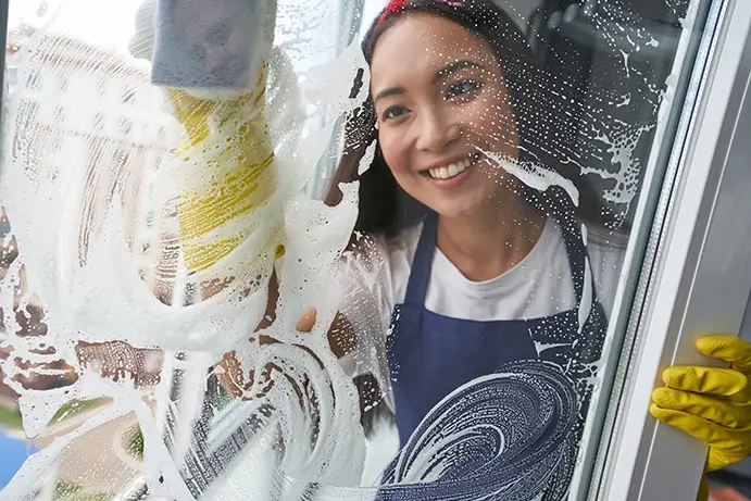 Une femme nettoie une fenêtre avec une éponge.
