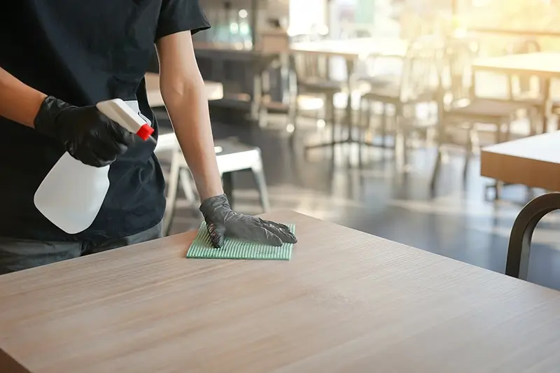 Une personne portant des gants noirs nettoie une table.